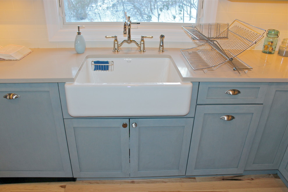 Example of a mountain style u-shaped light wood floor eat-in kitchen design in New York with a farmhouse sink, recessed-panel cabinets, blue cabinets, quartz countertops, white backsplash, ceramic backsplash and stainless steel appliances