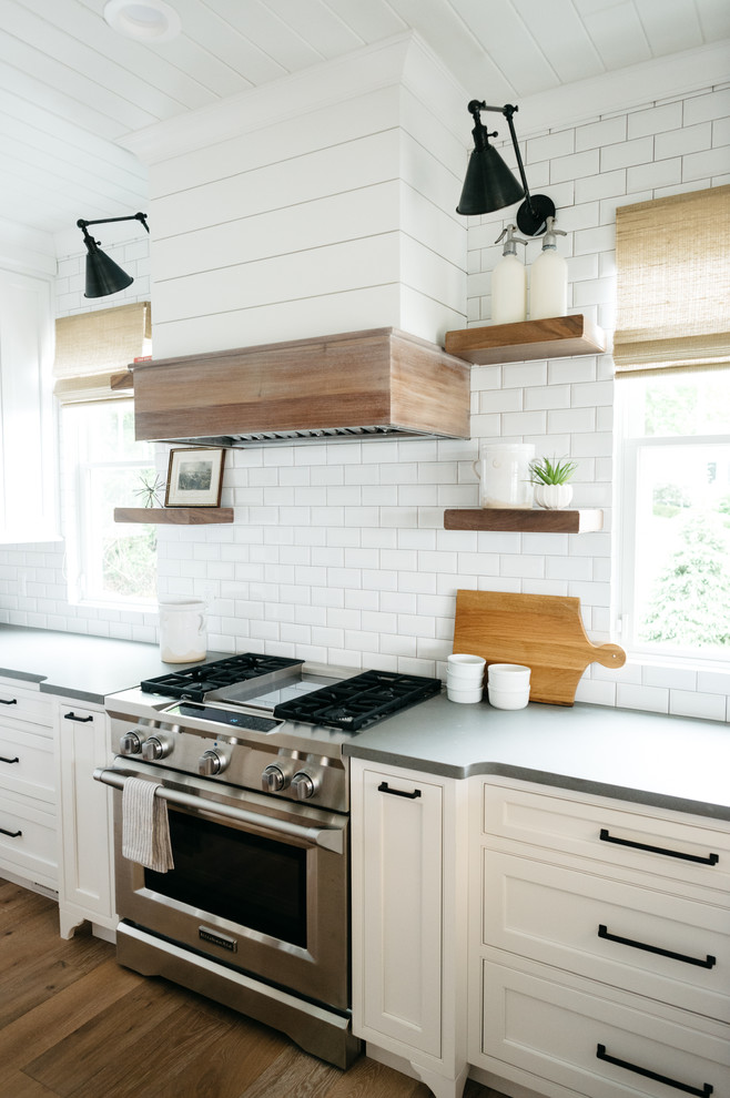 Lantlig inredning av ett mellanstort grå grått kök, med en rustik diskho, luckor med infälld panel, vita skåp, marmorbänkskiva, vitt stänkskydd, stänkskydd i tunnelbanekakel, mellanmörkt trägolv, en köksö och brunt golv