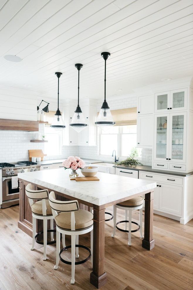 Exempel på ett mellanstort lantligt grå grått u-kök, med en rustik diskho, luckor med infälld panel, vita skåp, marmorbänkskiva, vitt stänkskydd, stänkskydd i tunnelbanekakel, mellanmörkt trägolv, en köksö och brunt golv