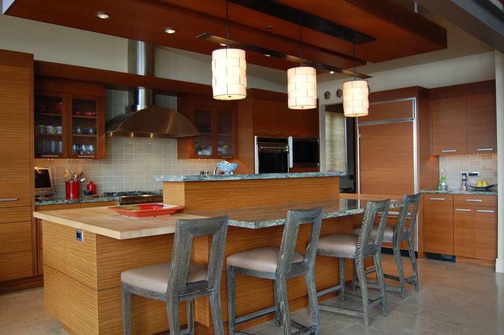 シアトルにある高級な広いコンテンポラリースタイルのおしゃれなキッチン (アンダーカウンターシンク、フラットパネル扉のキャビネット、中間色木目調キャビネット、ライムストーンカウンター、グレーのキッチンパネル、セラミックタイルのキッチンパネル、パネルと同色の調理設備、トラバーチンの床、ベージュの床、緑のキッチンカウンター) の写真