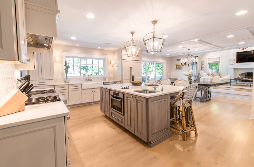 Example of a large transitional u-shaped light wood floor enclosed kitchen design in Milwaukee with a farmhouse sink, recessed-panel cabinets, porcelain backsplash, stainless steel appliances and an island