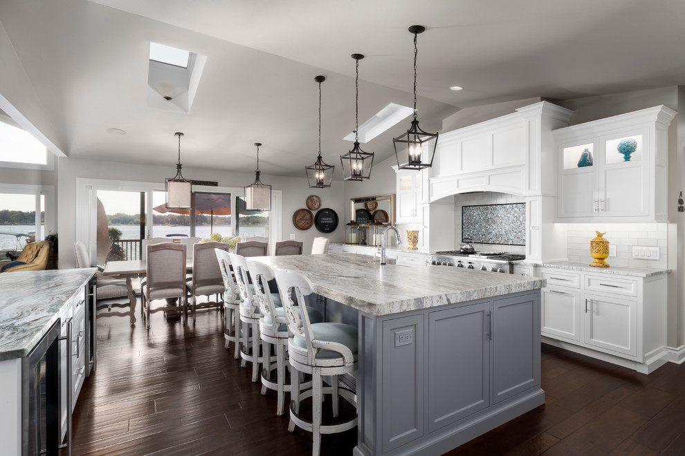 Large beach style l-shaped kitchen/diner in Detroit with a built-in sink, beaded cabinets, white cabinets, engineered stone countertops, white splashback, ceramic splashback, integrated appliances, dark hardwood flooring and an island.