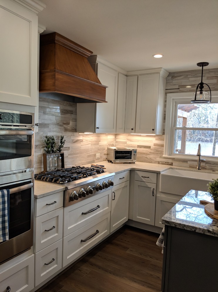 Mid-sized transitional laminate floor and brown floor eat-in kitchen photo in Other with a farmhouse sink, shaker cabinets, white cabinets, quartzite countertops, ceramic backsplash, stainless steel appliances, an island and white countertops