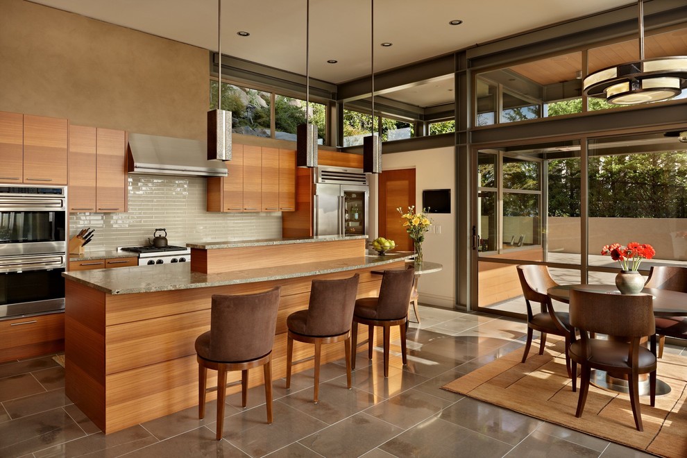 Idée de décoration pour une cuisine américaine minimaliste en bois brun avec une crédence beige, une crédence en carreau de verre, un électroménager en acier inoxydable et un placard à porte plane.