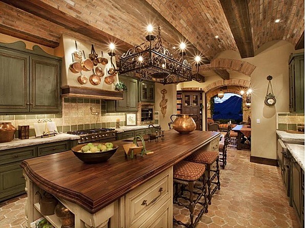 Eat-in kitchen - large mediterranean u-shaped terra-cotta tile eat-in kitchen idea in Las Vegas with raised-panel cabinets, distressed cabinets, an island, wood countertops, green backsplash, stone tile backsplash, a farmhouse sink and stainless steel appliances