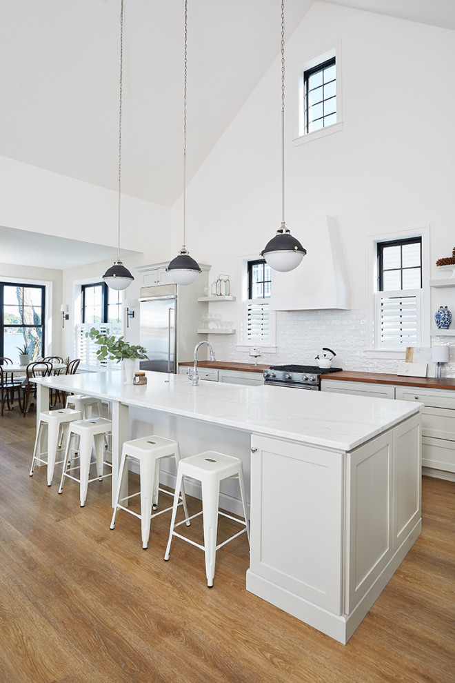 Design ideas for a coastal galley kitchen/diner in Grand Rapids with recessed-panel cabinets, white cabinets, marble worktops, white splashback, glass tiled splashback, stainless steel appliances, medium hardwood flooring, an island, brown floors and white worktops.