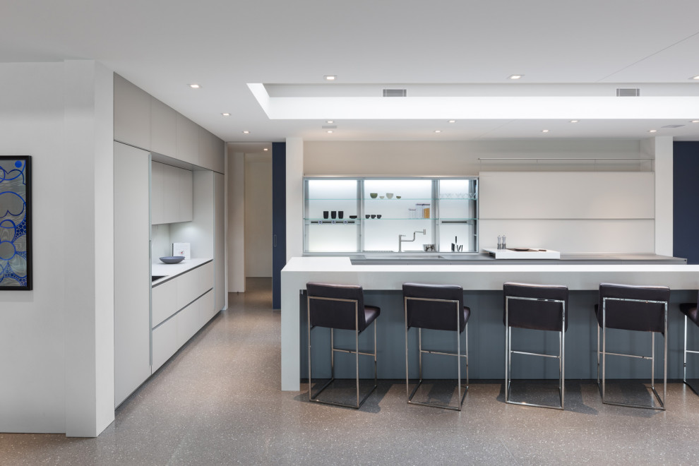 Идея дизайна: угловая кухня в стиле модернизм с плоскими фасадами, серыми фасадами, бетонным полом, островом, серым полом и белой столешницей