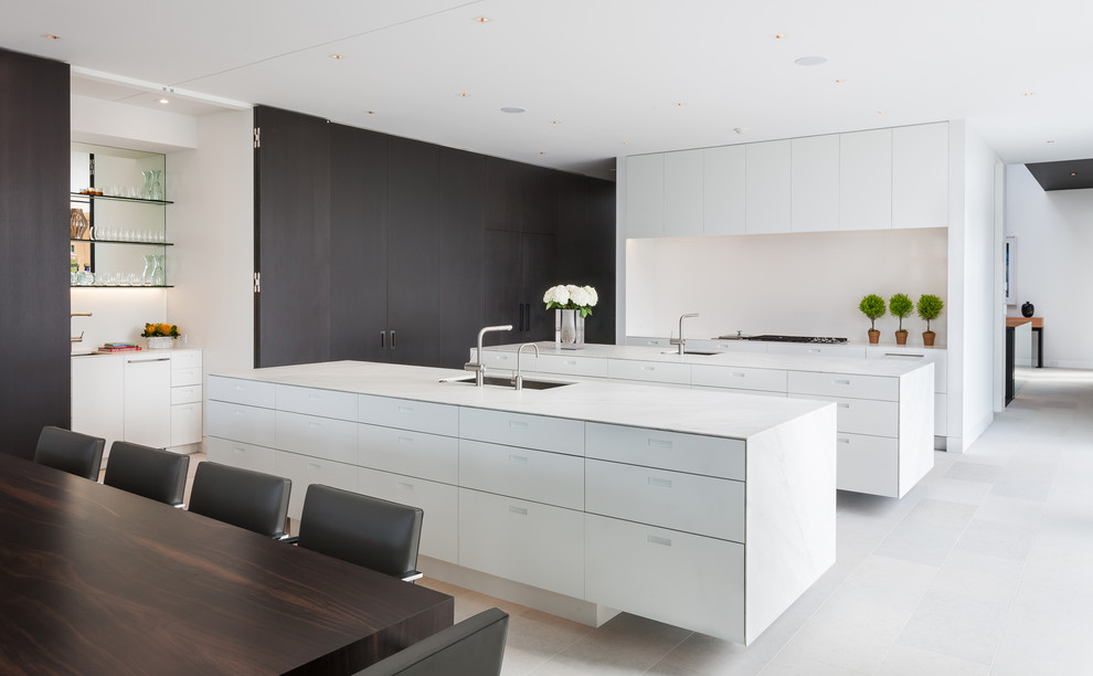 Inredning av ett modernt kök och matrum, med vitt golv, en undermonterad diskho, släta luckor, vita skåp, vitt stänkskydd och flera köksöar
