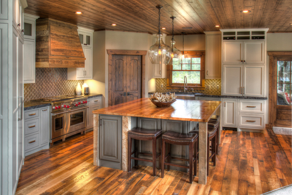 Inredning av ett rustikt mellanstort flerfärgad flerfärgat kök, med en rustik diskho, luckor med upphöjd panel, blå skåp, träbänkskiva, grått stänkskydd, stänkskydd i glaskakel, rostfria vitvaror, mellanmörkt trägolv, en köksö och flerfärgat golv