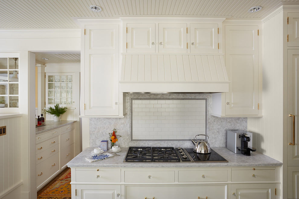 Foto på ett vintage kök, med en rustik diskho, luckor med upphöjd panel, vita skåp, bänkskiva i kvartsit, vitt stänkskydd, stänkskydd i porslinskakel, integrerade vitvaror, mellanmörkt trägolv och en halv köksö