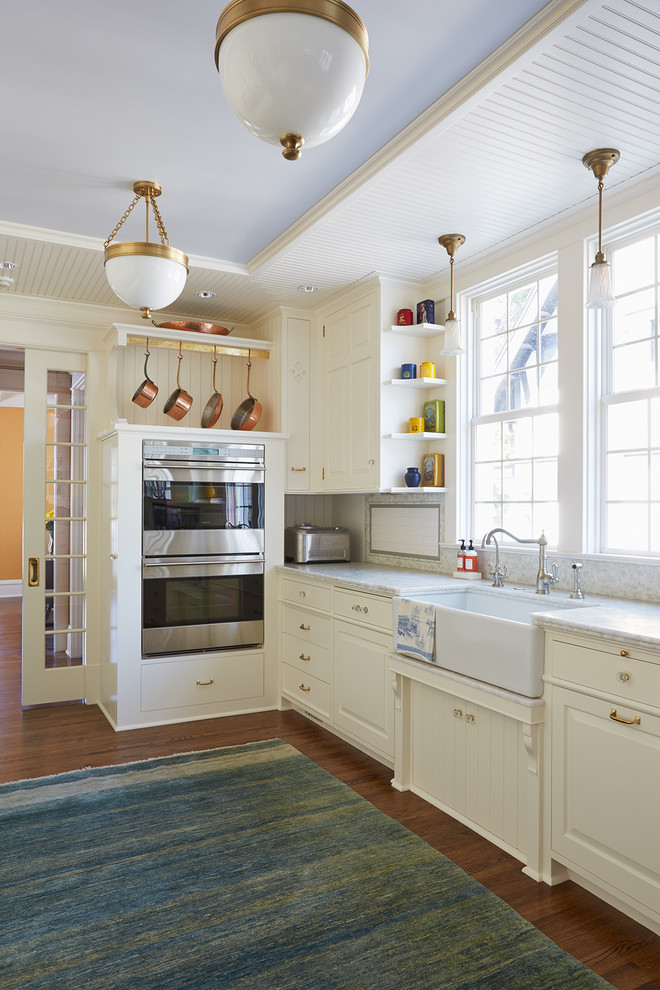 Klassisk inredning av ett kök, med en rustik diskho, luckor med upphöjd panel, vita skåp, bänkskiva i kvartsit, vitt stänkskydd, stänkskydd i porslinskakel, rostfria vitvaror och mörkt trägolv