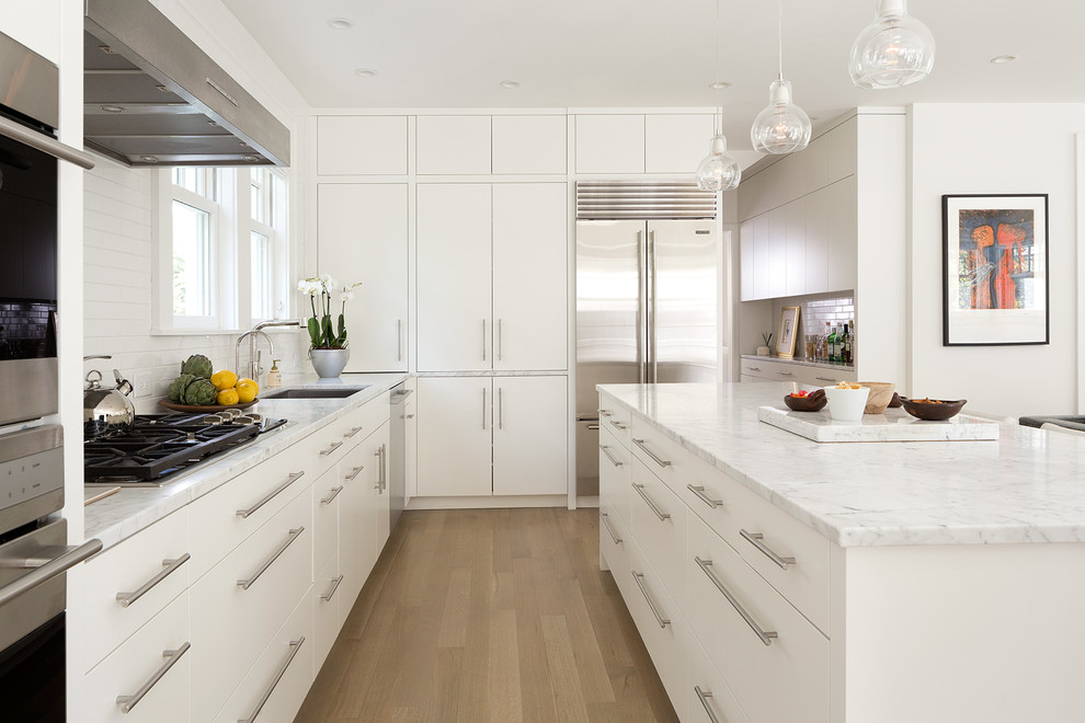 Design ideas for a contemporary l-shaped kitchen in Minneapolis with a submerged sink, flat-panel cabinets, white cabinets, white splashback, stainless steel appliances, light hardwood flooring and an island.