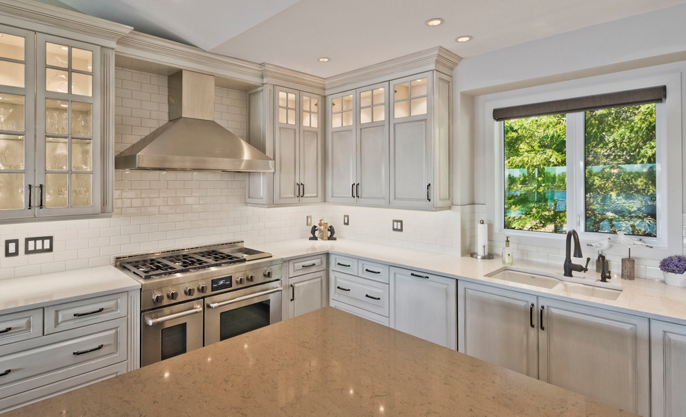 Large elegant u-shaped light wood floor and brown floor eat-in kitchen photo in Other with an undermount sink, raised-panel cabinets, gray cabinets, quartz countertops, white backsplash, porcelain backsplash, stainless steel appliances and an island