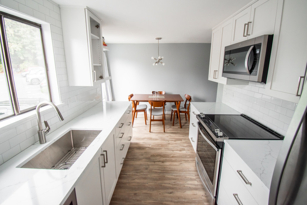 Example of a small trendy galley medium tone wood floor and brown floor eat-in kitchen design in Portland with an undermount sink, glass-front cabinets, white cabinets, white backsplash, ceramic backsplash, stainless steel appliances, no island, white countertops and quartzite countertops
