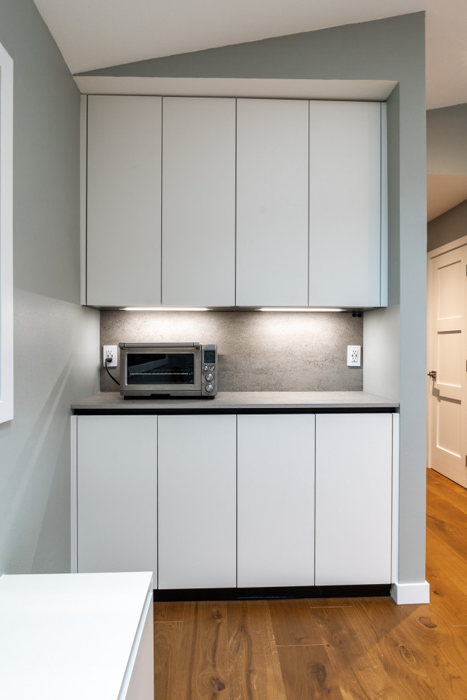 Modern inredning av ett mycket stort grå linjärt grått kök med öppen planlösning, med en undermonterad diskho, släta luckor, vita skåp, bänkskiva i kvarts, grått stänkskydd, integrerade vitvaror, mellanmörkt trägolv, flera köksöar och brunt golv