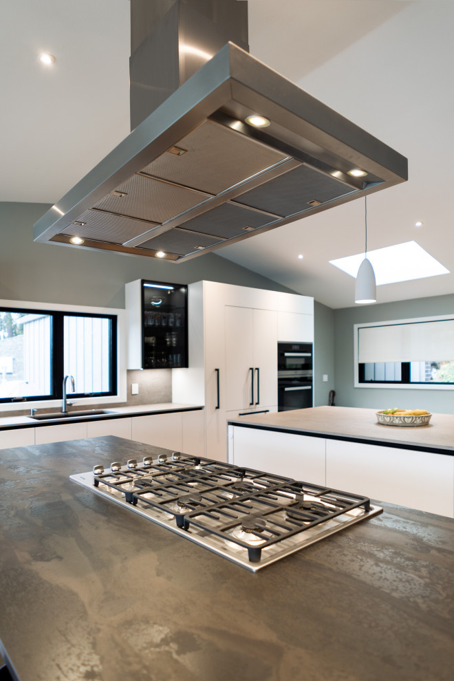 This is an example of an expansive modern single-wall open plan kitchen in Portland with a submerged sink, flat-panel cabinets, white cabinets, engineered stone countertops, grey splashback, engineered quartz splashback, integrated appliances, medium hardwood flooring, multiple islands, brown floors, grey worktops and a vaulted ceiling.