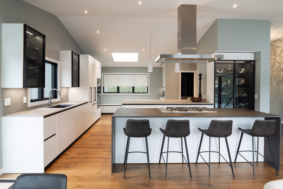 Exempel på ett mycket stort modernt grå linjärt grått kök med öppen planlösning, med en undermonterad diskho, släta luckor, vita skåp, bänkskiva i kvarts, grått stänkskydd, integrerade vitvaror, mellanmörkt trägolv, flera köksöar och brunt golv