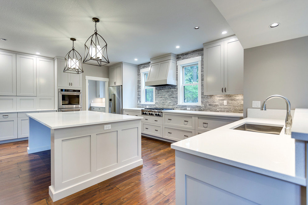 Large transitional u-shaped medium tone wood floor and brown floor open concept kitchen photo in Portland with an undermount sink, shaker cabinets, white cabinets, quartz countertops, gray backsplash, marble backsplash, stainless steel appliances and an island