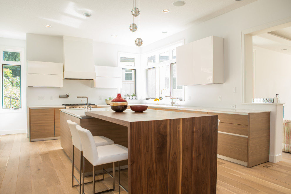 Contemporary kitchen/diner in Portland with a submerged sink, flat-panel cabinets, light wood cabinets, engineered stone countertops, integrated appliances, light hardwood flooring and an island.