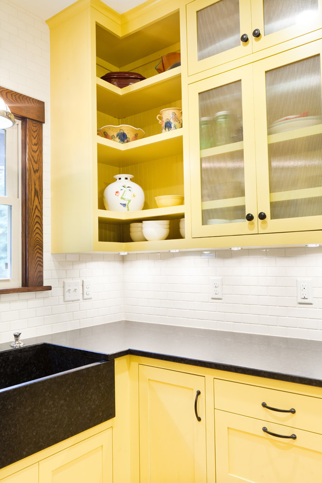 Example of a mid-sized classic u-shaped light wood floor eat-in kitchen design in Minneapolis with a farmhouse sink, flat-panel cabinets, yellow cabinets, granite countertops, white backsplash, ceramic backsplash, black appliances and no island