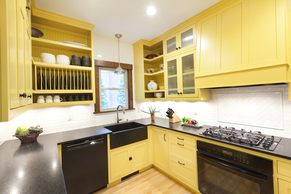 Example of a mid-sized classic l-shaped light wood floor eat-in kitchen design in Minneapolis with a farmhouse sink, yellow cabinets, granite countertops, white backsplash, ceramic backsplash, black appliances, shaker cabinets and no island