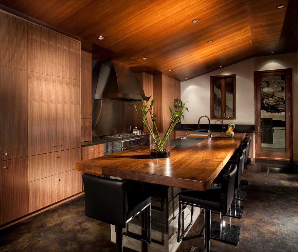 На фото: кухня в современном стиле с плоскими фасадами, фасадами цвета дерева среднего тона, деревянной столешницей и техникой из нержавеющей стали