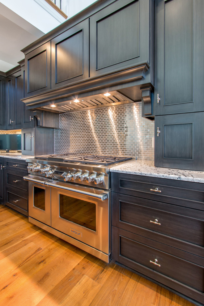 Eat-in kitchen - large traditional l-shaped light wood floor eat-in kitchen idea in Milwaukee with a single-bowl sink, recessed-panel cabinets, dark wood cabinets, granite countertops, metallic backsplash, metal backsplash, paneled appliances and an island