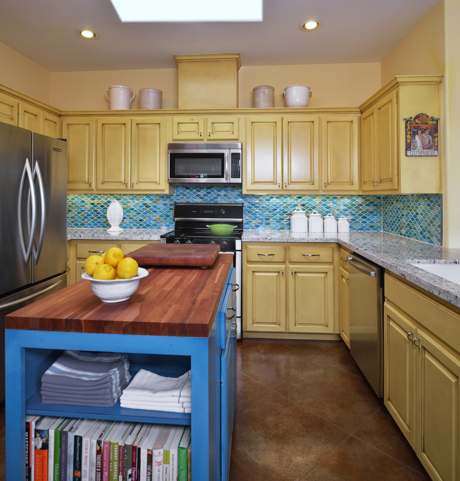 Idéer för ett mellanstort klassiskt kök, med en undermonterad diskho, luckor med upphöjd panel, gula skåp, blått stänkskydd, rostfria vitvaror, granitbänkskiva, betonggolv och en köksö