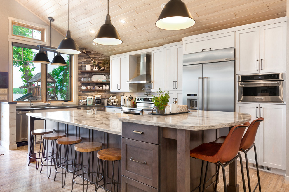 Idéer för ett rustikt beige l-kök, med skåp i shakerstil, vita skåp, rostfria vitvaror, mellanmörkt trägolv, en köksö och brunt golv