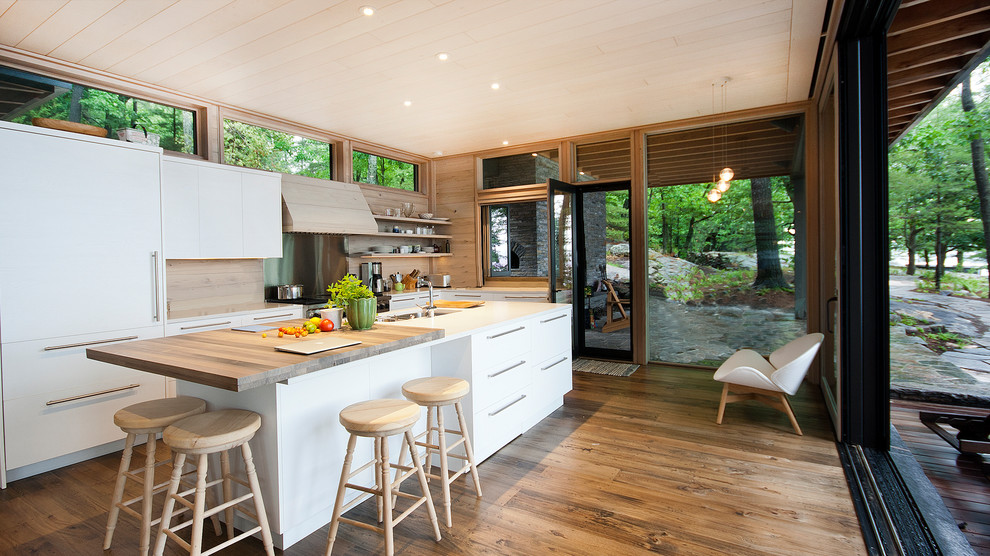 Large rustic l-shaped kitchen in Toronto with a submerged sink, flat-panel cabinets, white cabinets, medium hardwood flooring, an island, brown floors, wood splashback, stainless steel appliances, white worktops and a wood ceiling.