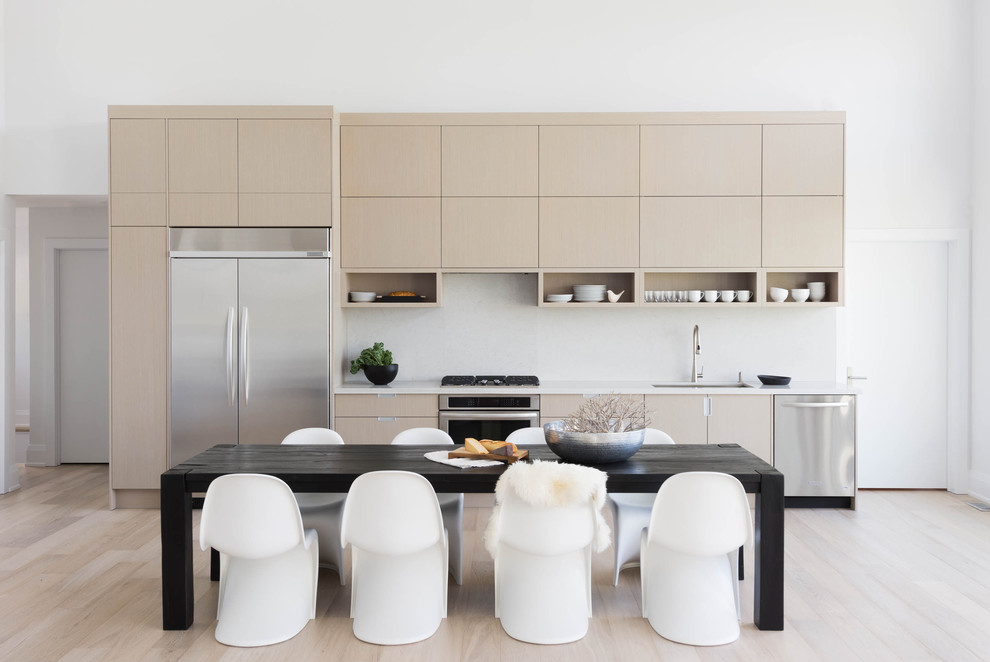 Immagine di una cucina scandinava con ante lisce, ante in legno chiaro, paraspruzzi bianco, elettrodomestici in acciaio inossidabile e parquet chiaro