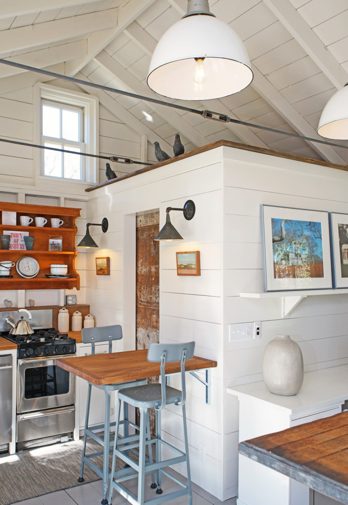 Modelo de cocina de estilo de casa de campo con puertas de armario blancas, encimera de madera, electrodomésticos de acero inoxidable y suelo gris