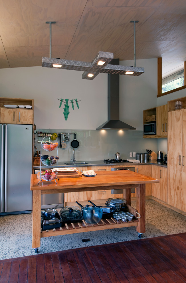 Foto på ett rustikt l-kök, med en nedsänkt diskho, släta luckor, skåp i ljust trä, bänkskiva i rostfritt stål, glaspanel som stänkskydd, rostfria vitvaror och en köksö