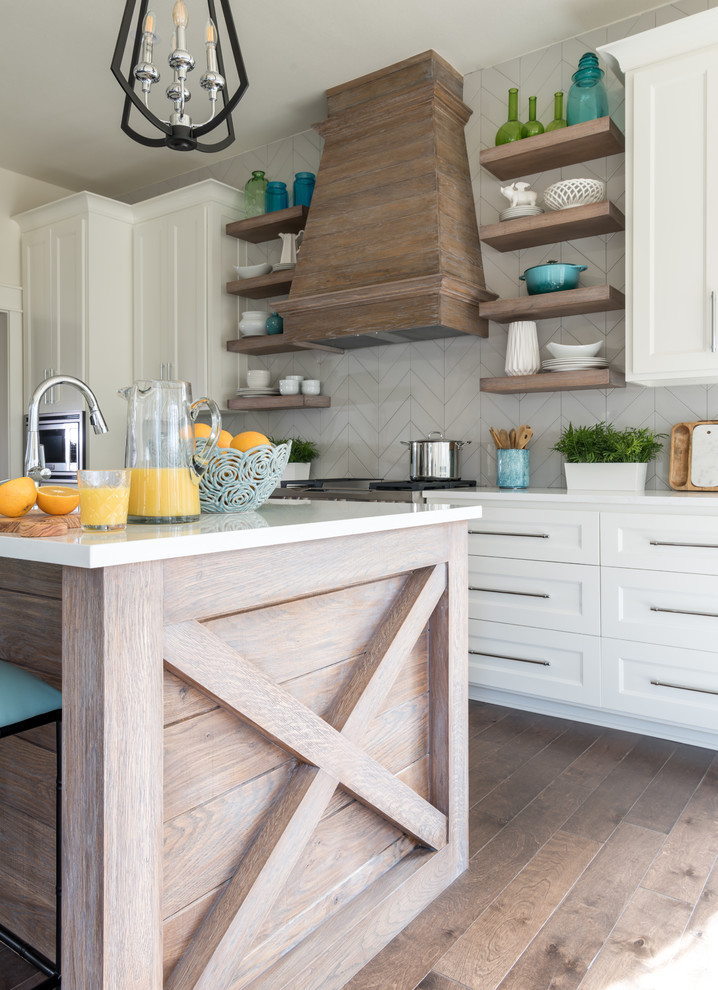 Example of a mid-sized beach style l-shaped medium tone wood floor and brown floor open concept kitchen design with a farmhouse sink, shaker cabinets, white cabinets, quartz countertops, gray backsplash, ceramic backsplash, stainless steel appliances and an island