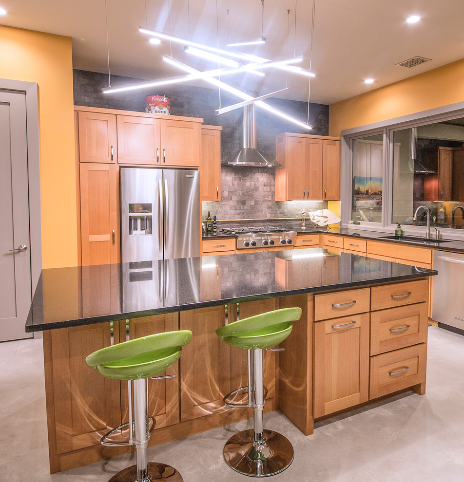 Mid-sized trendy l-shaped concrete floor open concept kitchen photo in Austin with medium tone wood cabinets, laminate countertops, stainless steel appliances, an island, an undermount sink, shaker cabinets, gray backsplash and stone tile backsplash