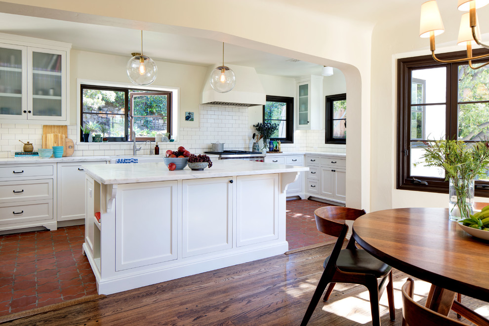 Large tuscan l-shaped terra-cotta tile eat-in kitchen photo in Los Angeles with a farmhouse sink, beaded inset cabinets, white cabinets, marble countertops, white backsplash, ceramic backsplash, stainless steel appliances and an island