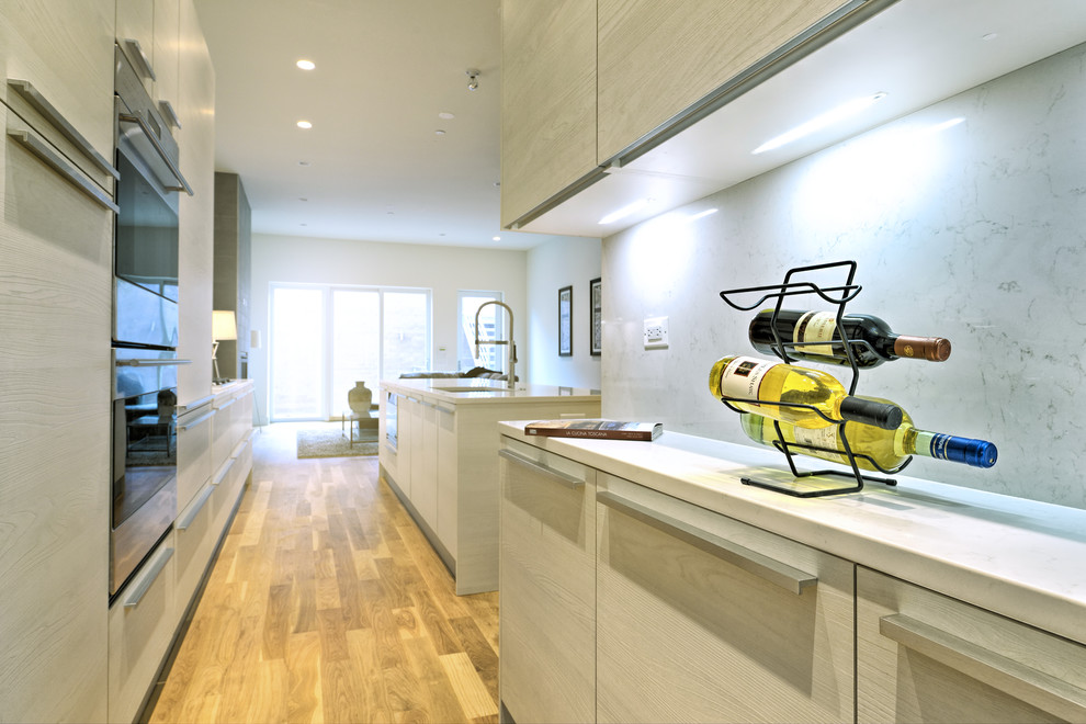 Contemporary galley kitchen/diner in Chicago with a submerged sink, flat-panel cabinets, light wood cabinets, engineered stone countertops, white splashback, integrated appliances, light hardwood flooring and an island.