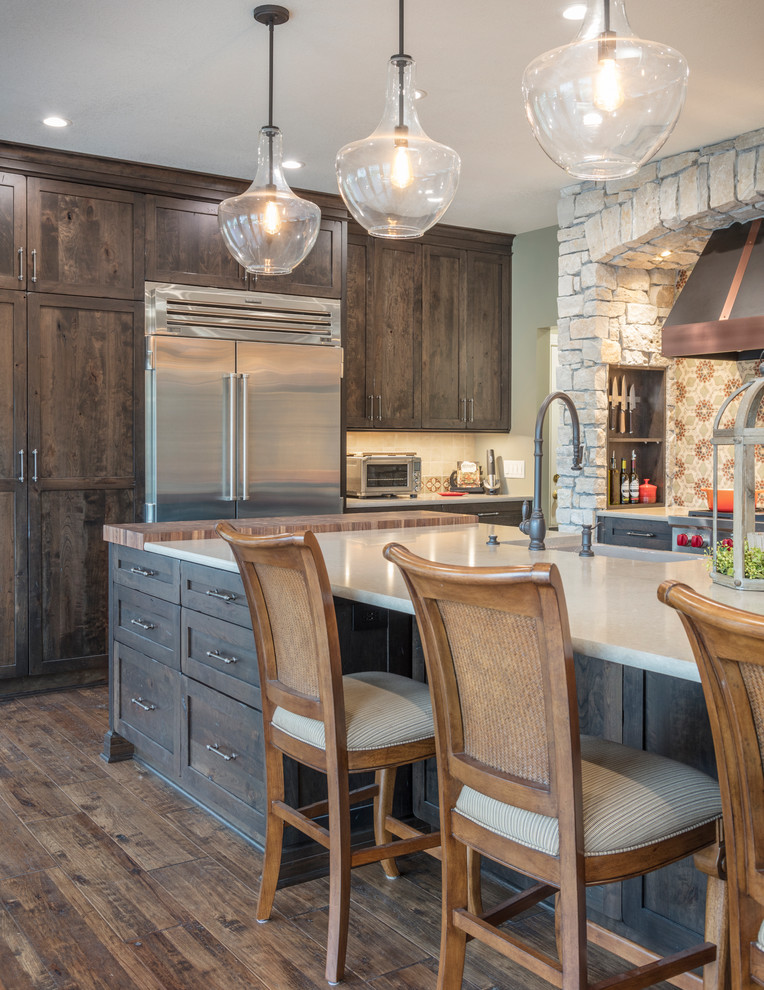 Inspiration for a medium sized rustic open plan kitchen in Kansas City with a belfast sink, shaker cabinets, distressed cabinets, engineered stone countertops, multi-coloured splashback, terracotta splashback, stainless steel appliances, medium hardwood flooring, an island and brown floors.