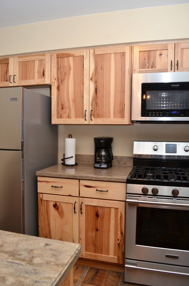 Medium sized rustic l-shaped kitchen/diner in Other with shaker cabinets, medium wood cabinets, composite countertops, a breakfast bar, beige worktops, a submerged sink, stainless steel appliances, medium hardwood flooring and brown floors.