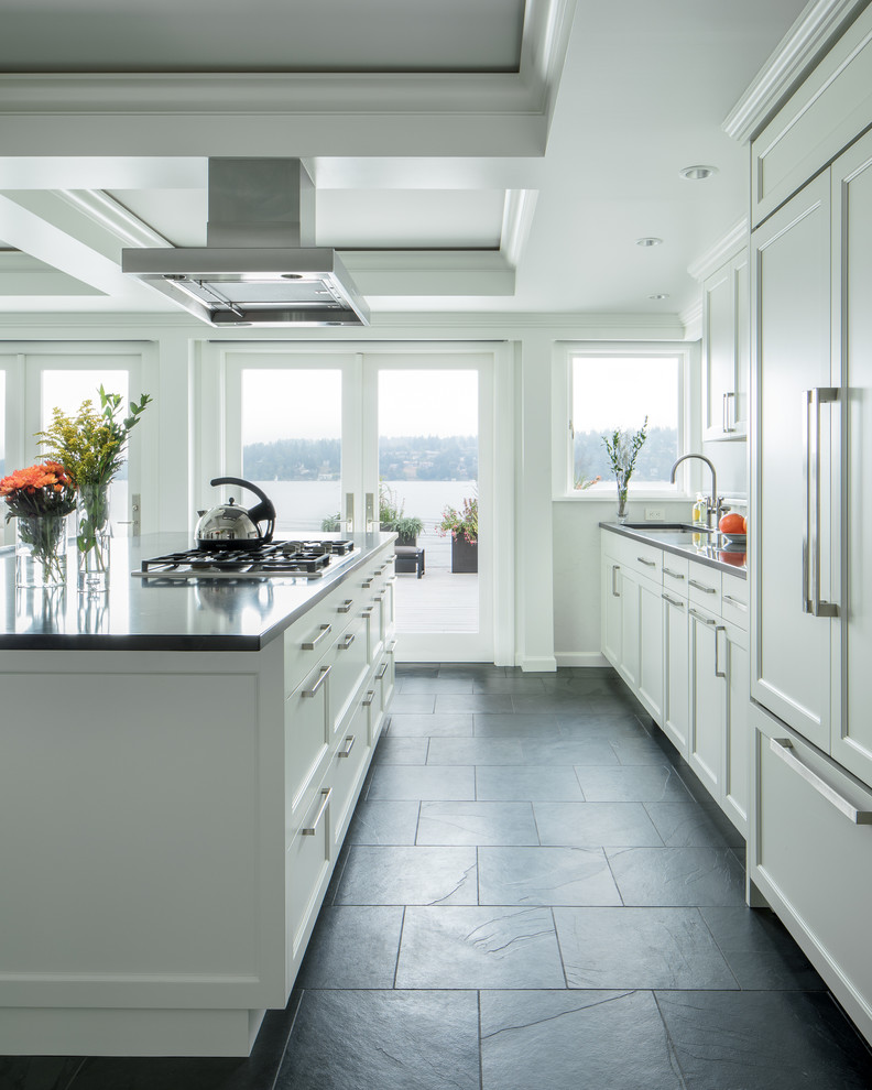 Inspiration for a traditional galley kitchen in Seattle with a submerged sink, recessed-panel cabinets, white cabinets, engineered stone countertops, white splashback, integrated appliances, slate flooring, an island, black floors and grey worktops.