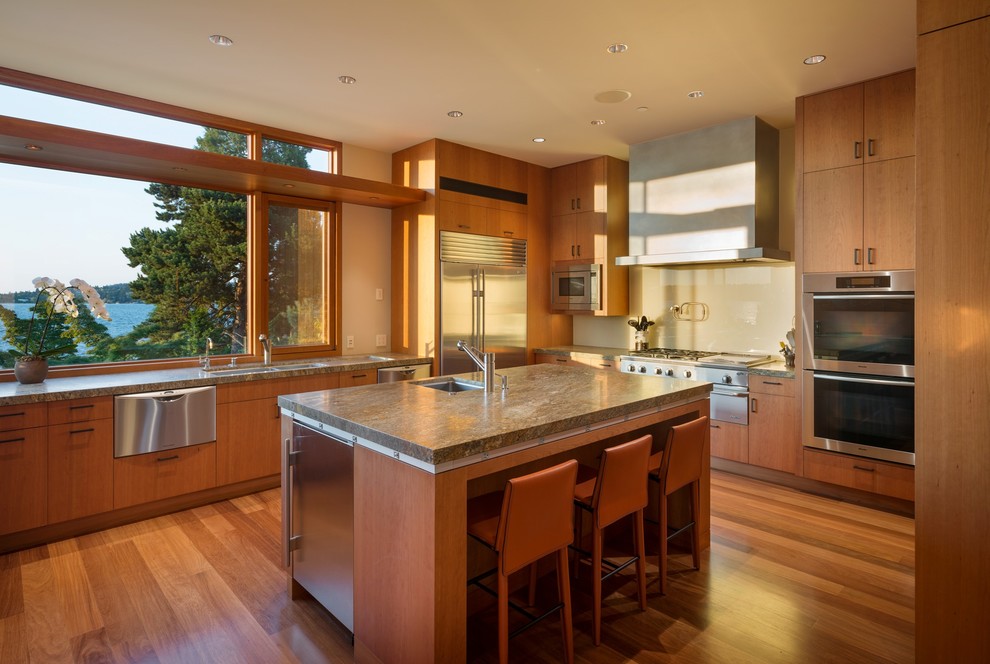 Large trendy l-shaped medium tone wood floor kitchen photo in Seattle with a double-bowl sink, flat-panel cabinets, medium tone wood cabinets, granite countertops, beige backsplash, glass sheet backsplash, stainless steel appliances and an island