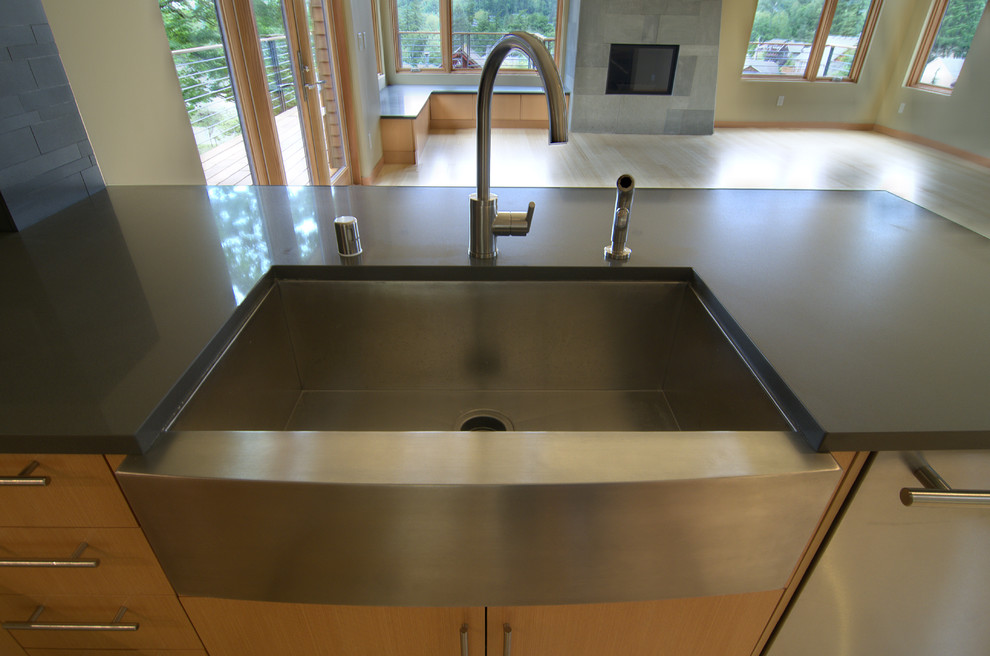 This is an example of a large contemporary galley open plan kitchen in Seattle with a belfast sink, flat-panel cabinets, medium wood cabinets, composite countertops, black splashback, stone tiled splashback, stainless steel appliances and a breakfast bar.