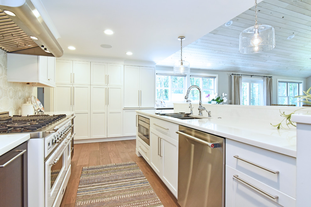 Inredning av ett klassiskt mellanstort vit vitt kök, med en undermonterad diskho, luckor med infälld panel, vita skåp, rostfria vitvaror, mörkt trägolv, brunt golv, bänkskiva i kvarts, grått stänkskydd, stänkskydd i keramik och en köksö