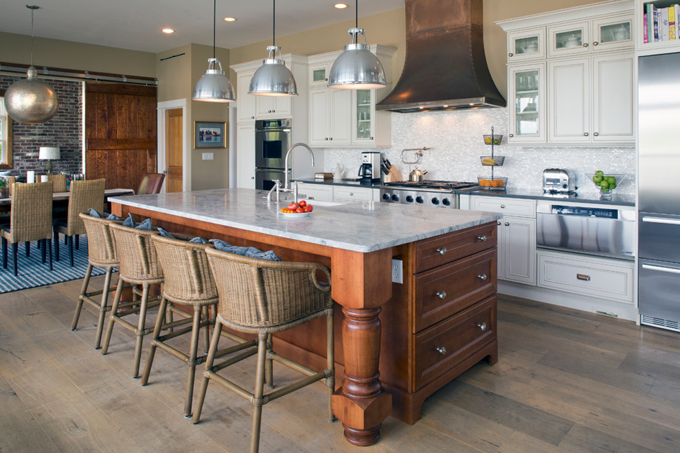 Eat-in kitchen - large coastal galley medium tone wood floor eat-in kitchen idea in New York with a farmhouse sink, white cabinets, marble countertops, white backsplash, glass tile backsplash, stainless steel appliances, an island and recessed-panel cabinets