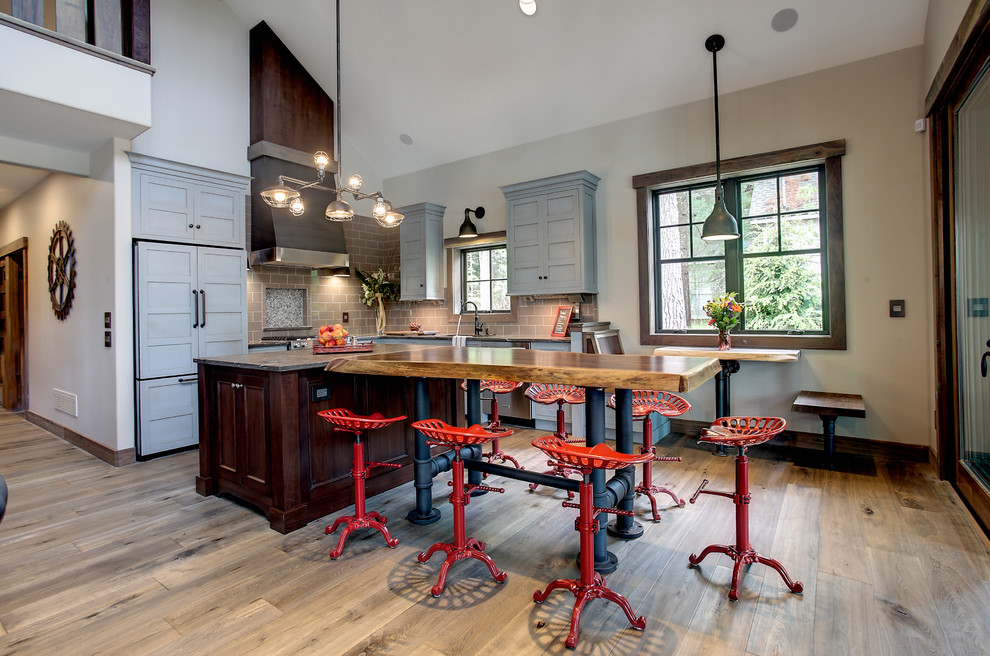 Bild på ett mellanstort amerikanskt kök, med en undermonterad diskho, luckor med profilerade fronter, blå skåp, granitbänkskiva, brunt stänkskydd, stänkskydd i tunnelbanekakel, rostfria vitvaror, mellanmörkt trägolv och en köksö
