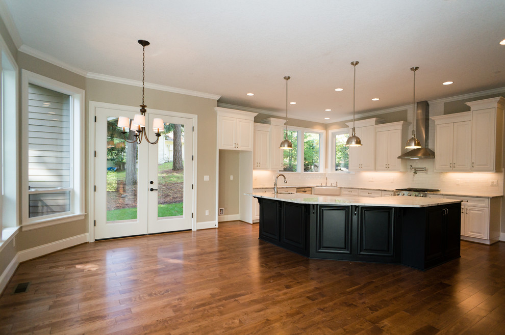Example of a large transitional l-shaped medium tone wood floor open concept kitchen design in Portland with a farmhouse sink, recessed-panel cabinets, white cabinets, granite countertops, white backsplash, subway tile backsplash, stainless steel appliances and an island