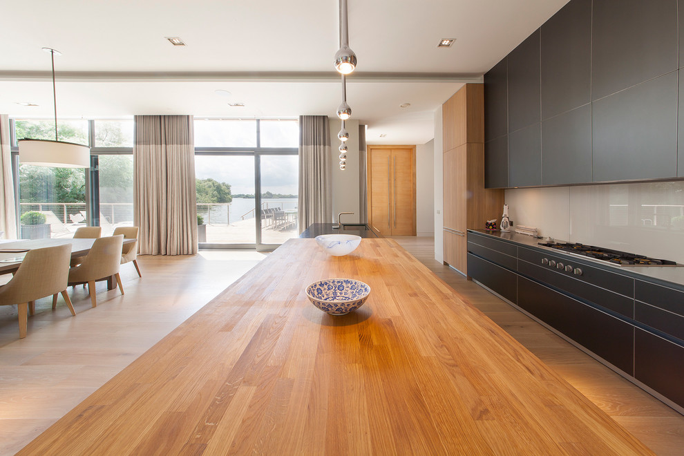 Expansive contemporary open plan kitchen in Surrey with light hardwood flooring, an island, a submerged sink and wood worktops.