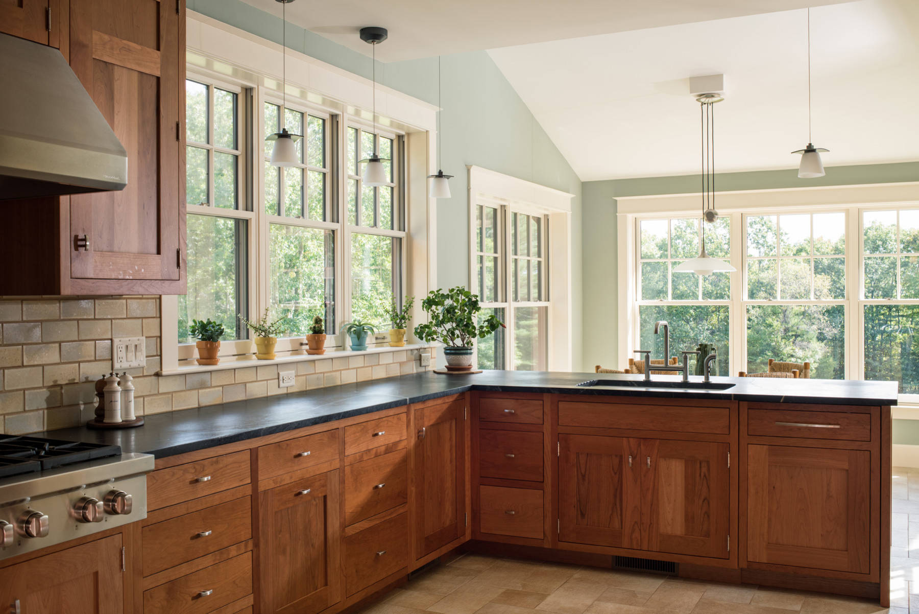 Inspiration for a craftsman beige floor kitchen remodel in Boston with an undermount sink, green cabinets, beige backsplash, stainless steel appliances, a peninsula and black countertops