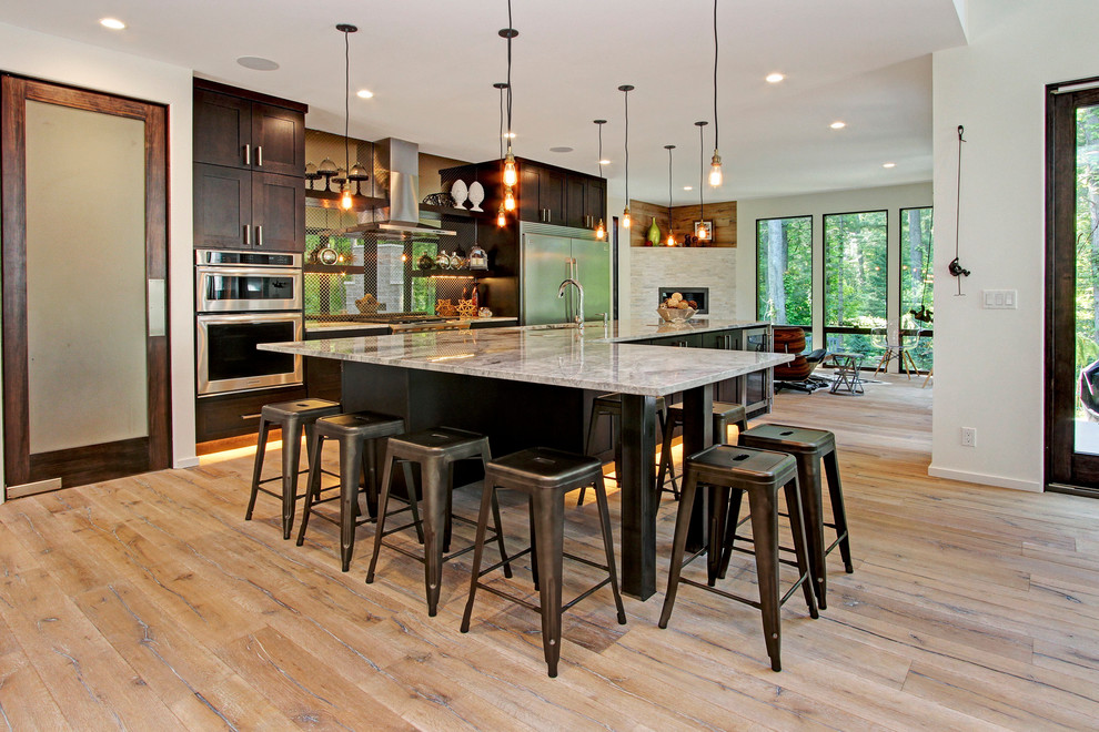 This is an example of a large contemporary galley kitchen/diner in Grand Rapids with a submerged sink, shaker cabinets, dark wood cabinets, granite worktops, mirror splashback, stainless steel appliances, light hardwood flooring and an island.
