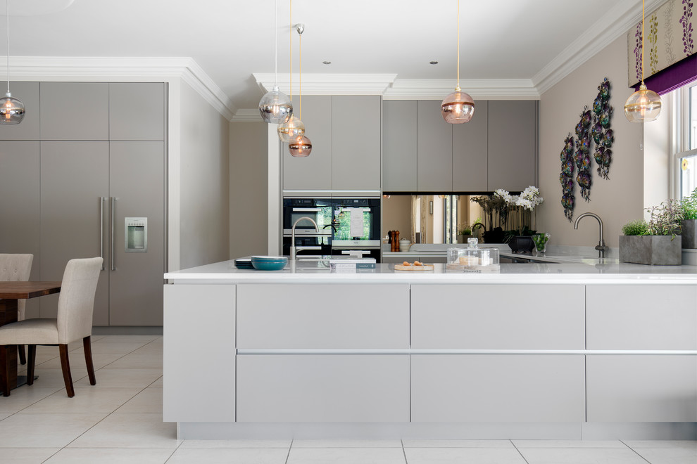This is an example of a large traditional u-shaped open plan kitchen in Surrey with a submerged sink, flat-panel cabinets, white cabinets, composite countertops, metallic splashback, glass sheet splashback, integrated appliances, cement flooring and beige floors.